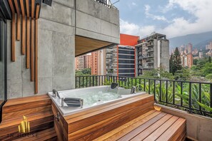 A modern outdoor hot tub area with a wooden deck and a city view. - Elevated Living: Balcony, AC - Morph 702 (Medellín)