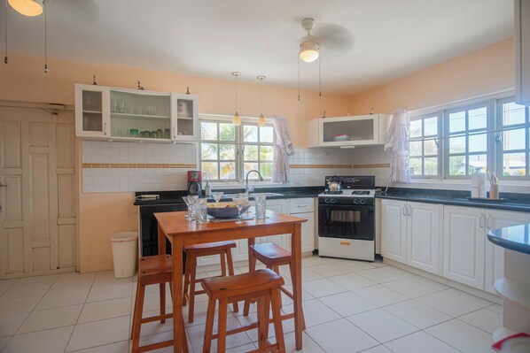 A kitchen with white cabinets, a wooden table with stools, a microwave, an oven, and a window with curtains.