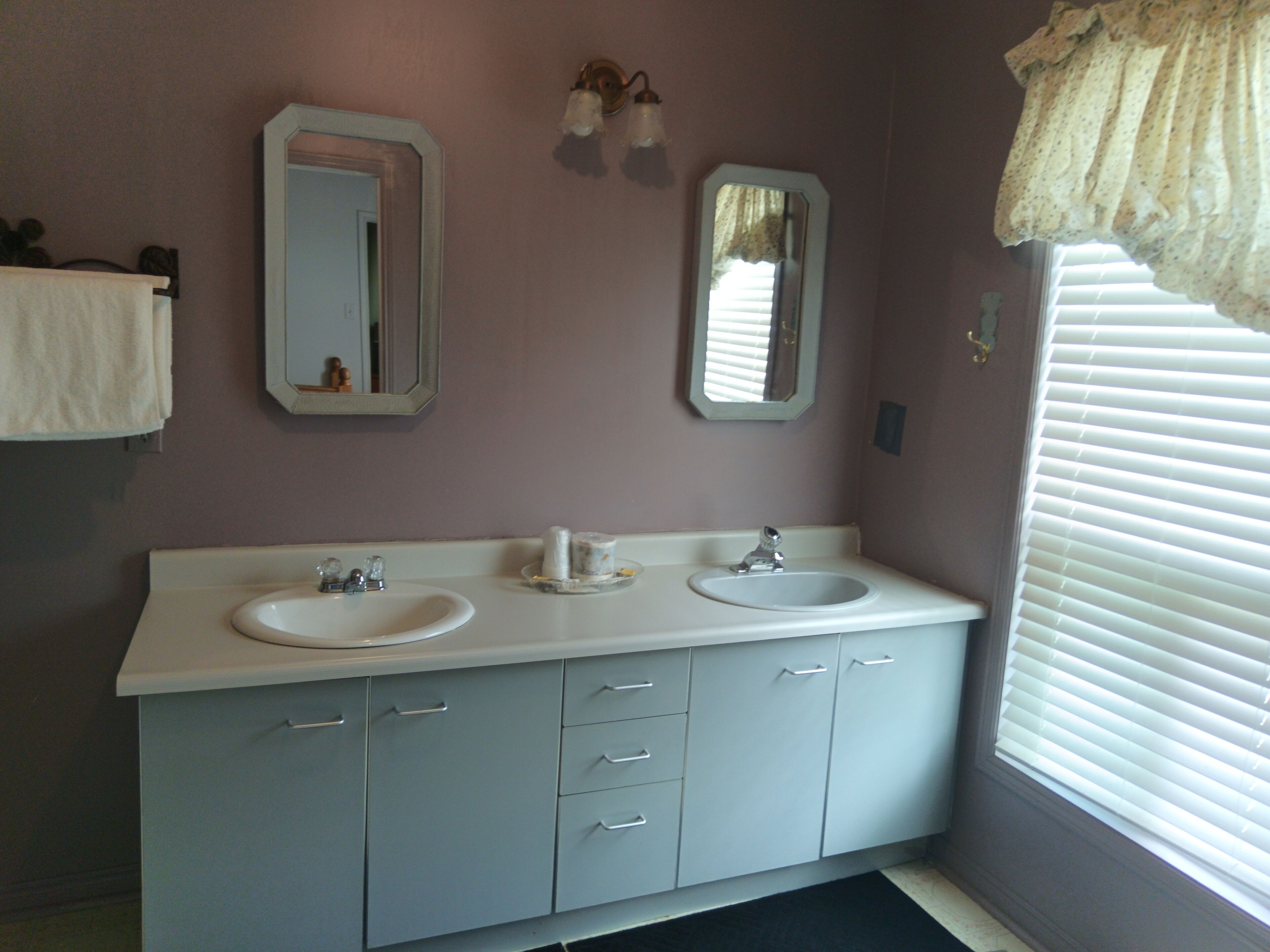 A bathroom with two sinks, a mirror, and a window with blinds.