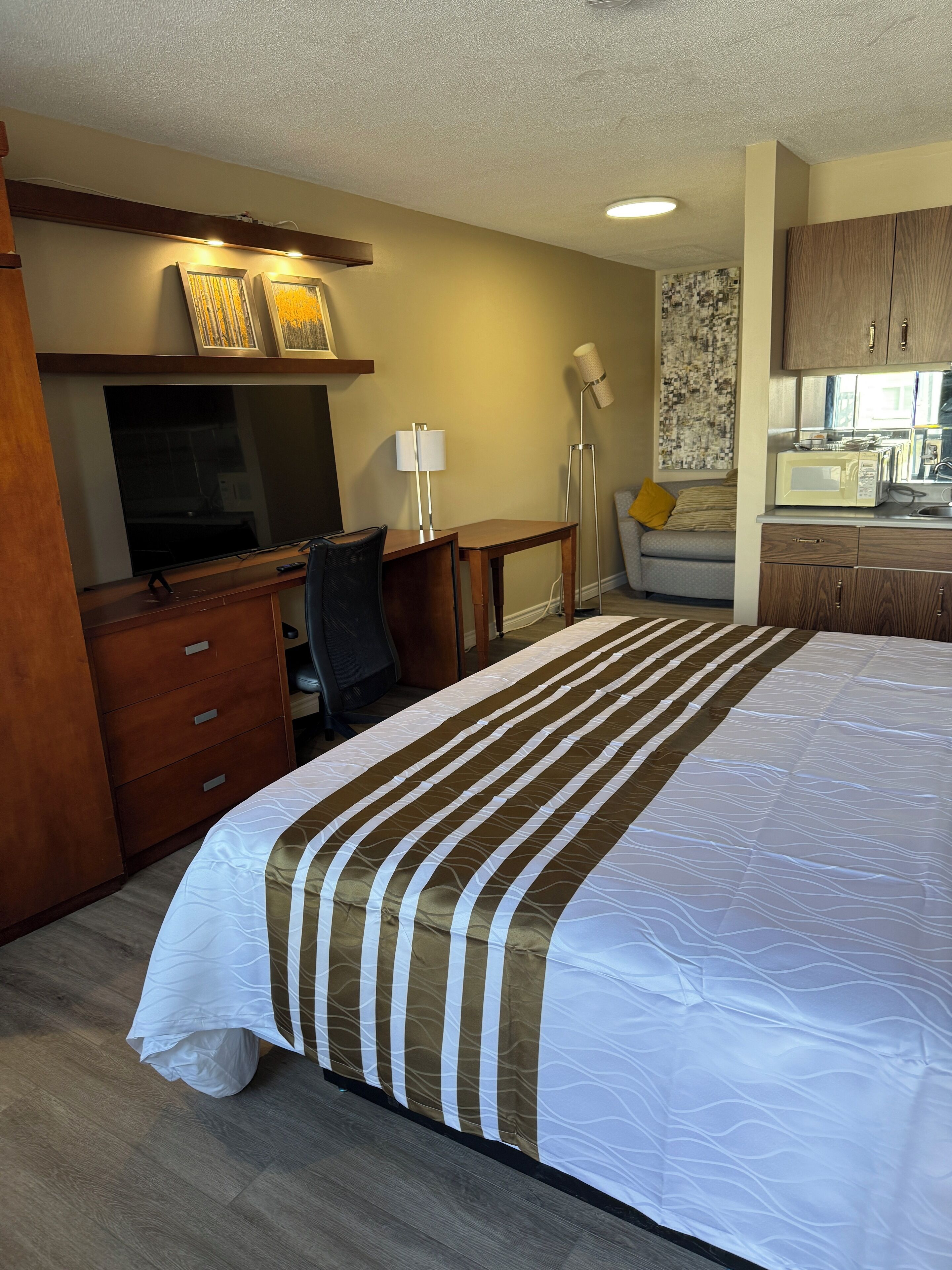 Hotelkamer met een groot bed, een bureau met stoel, een flatscreen televisie, een lamp en een kitchenette.