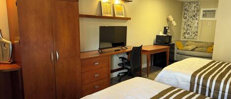 Habitación de hotel con dos camas, un escritorio con computadora, una silla, un armario y un sofá.