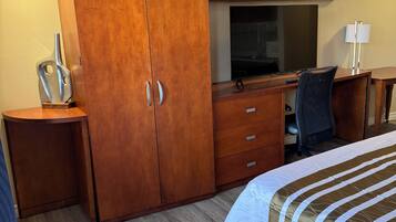 Ein Hotelzimmer mit Holzschrank, Schreibtisch mit Computer, Fernseher und Bett mit gestreifter Bettwäsche.