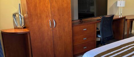 Une chambre d’hôtel avec une armoire en bois, un bureau avec un ordinateur, une télévision et un lit avec une literie à rayures.