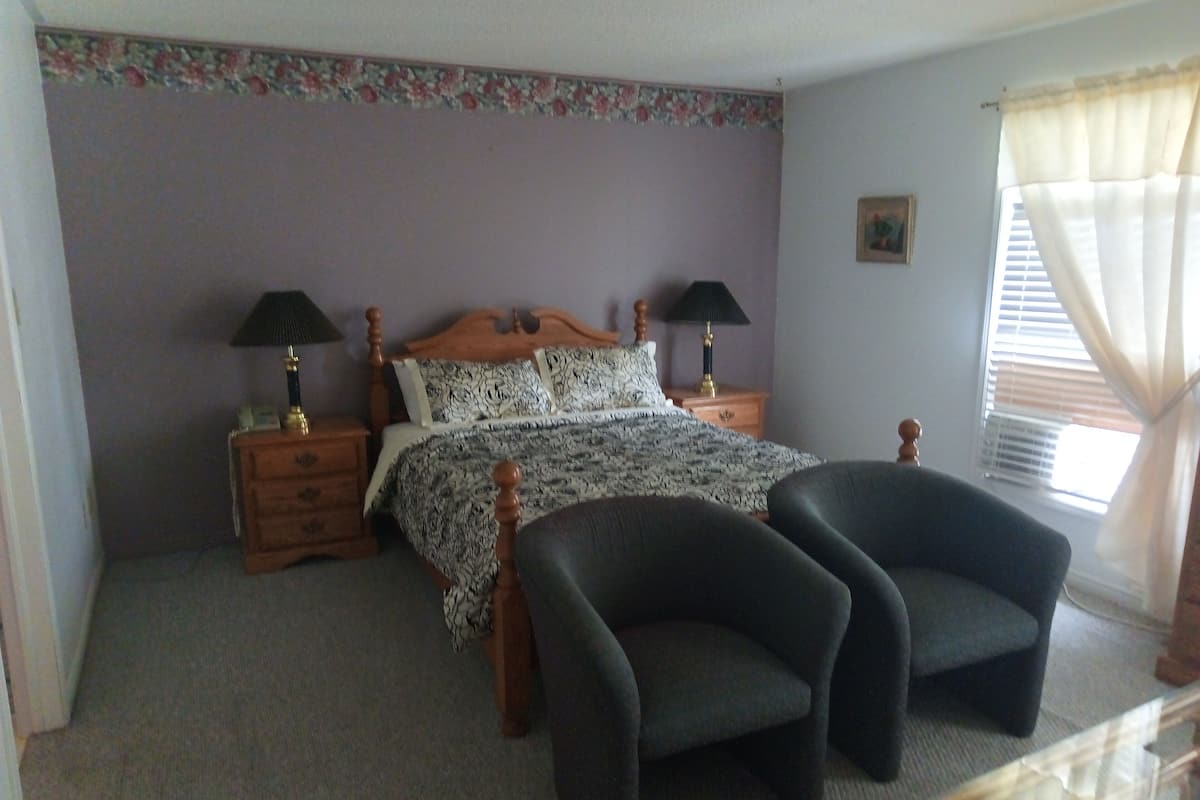 A bedroom with a bed, two nightstands, two lamps, a chair, and a window with curtains.