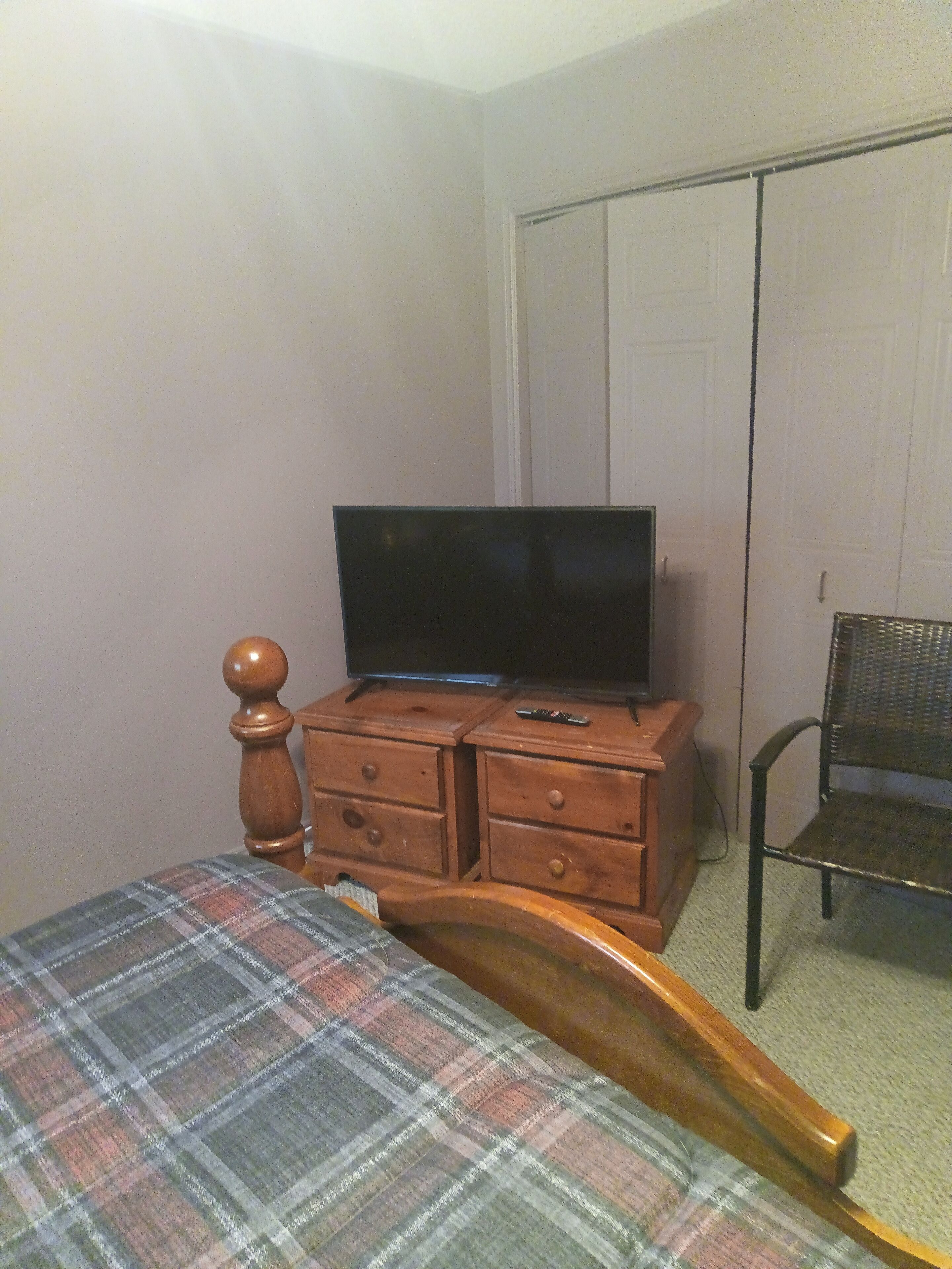A bedroom with a bed, a wooden dresser with a television, a chair, and a closet.
