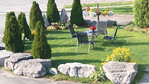 A garden with a table and chairs, surrounded by rocks and trimmed bushes. - Princess Motel  (Kawartha Lakes)
