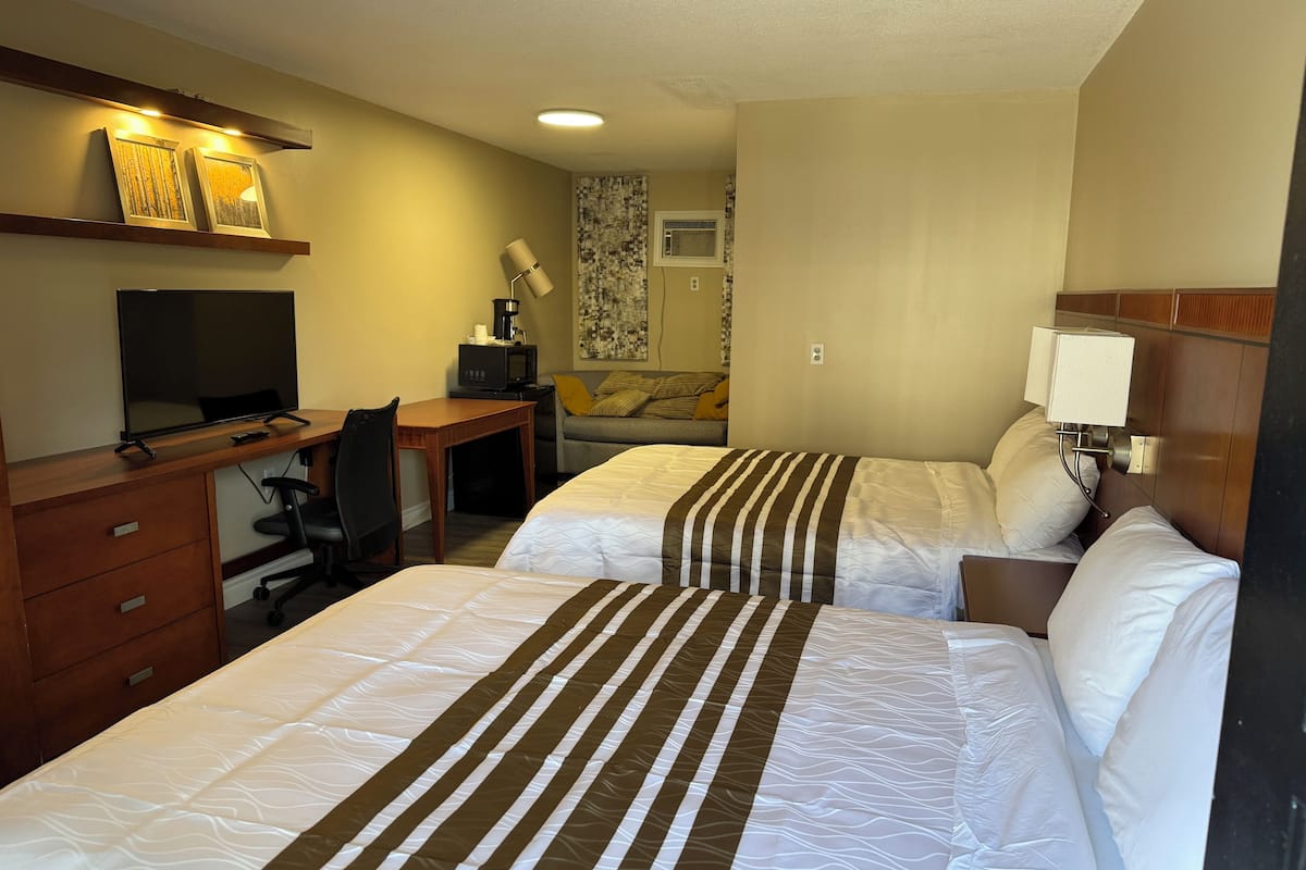 A hotel room with two beds, a desk with a computer, a TV, and a microwave.