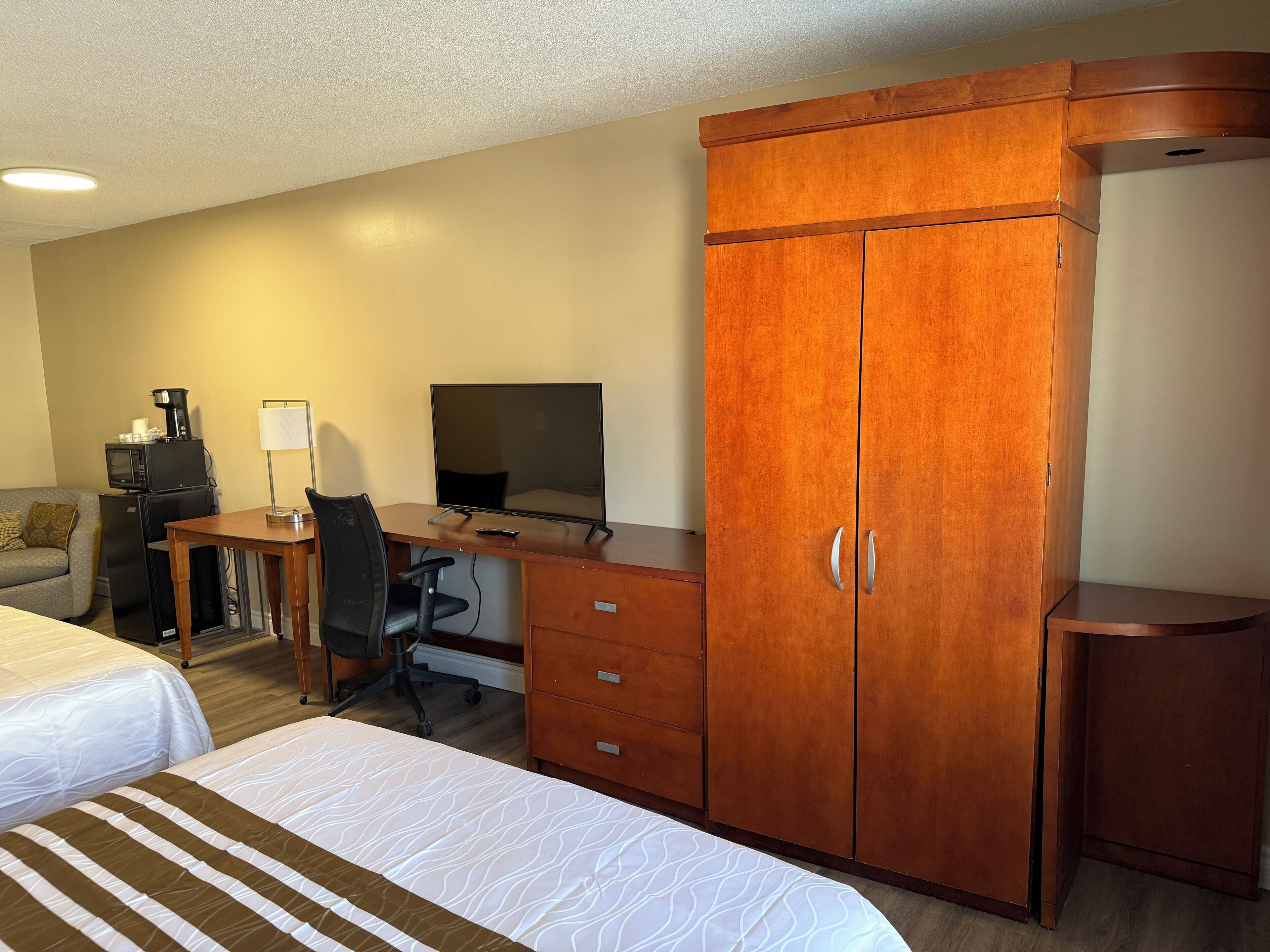 A hotel room with two beds, a desk with a computer, a microwave, a coffee maker, a TV, and a wardrobe.