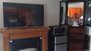 A living room with a flat-screen TV, a fireplace, a refrigerator, and a wooden cabinet. - Princess Motel  (Kawartha Lakes)