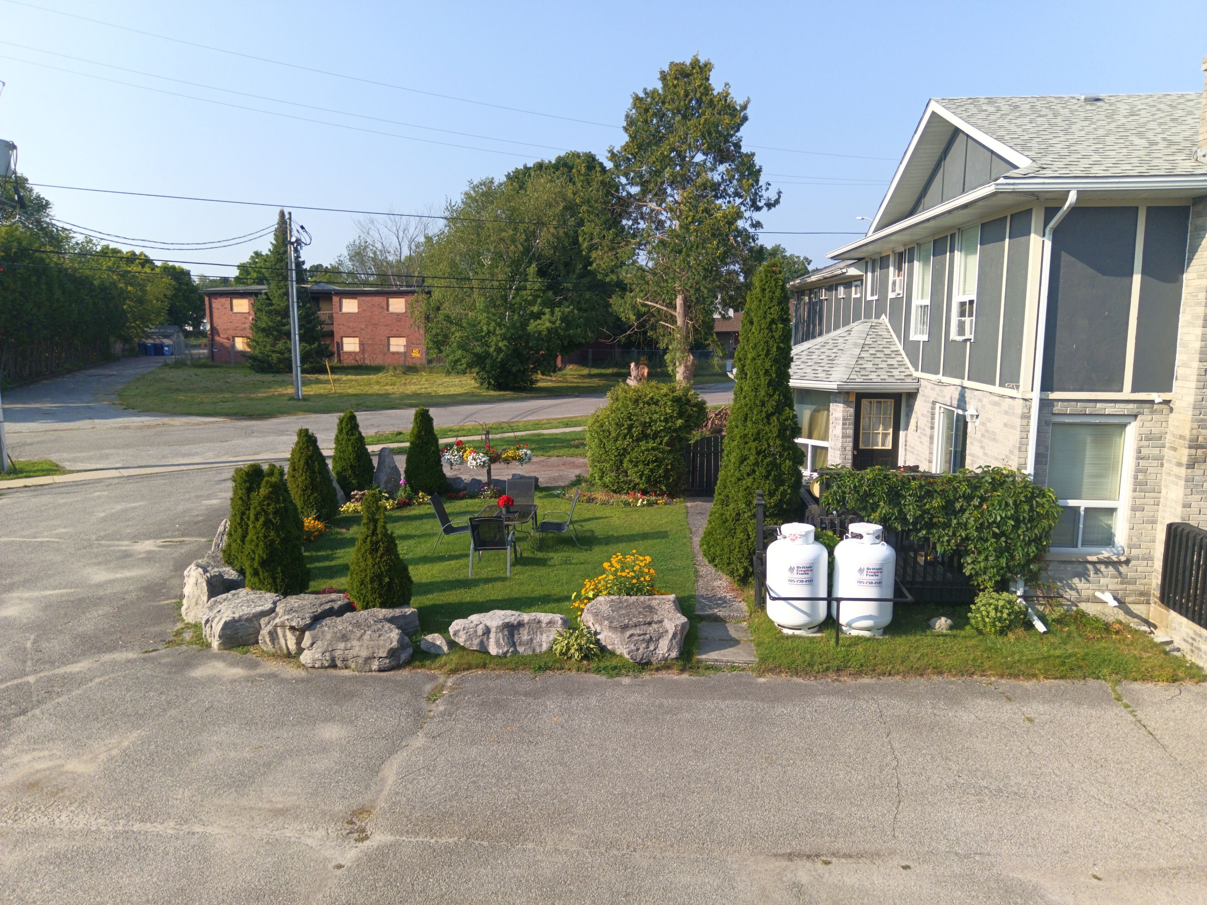 Un quartier résidentiel avec une pelouse bien entretenue, une terrasse avec des chaises et deux réservoirs de propane situés sur le côté droit.