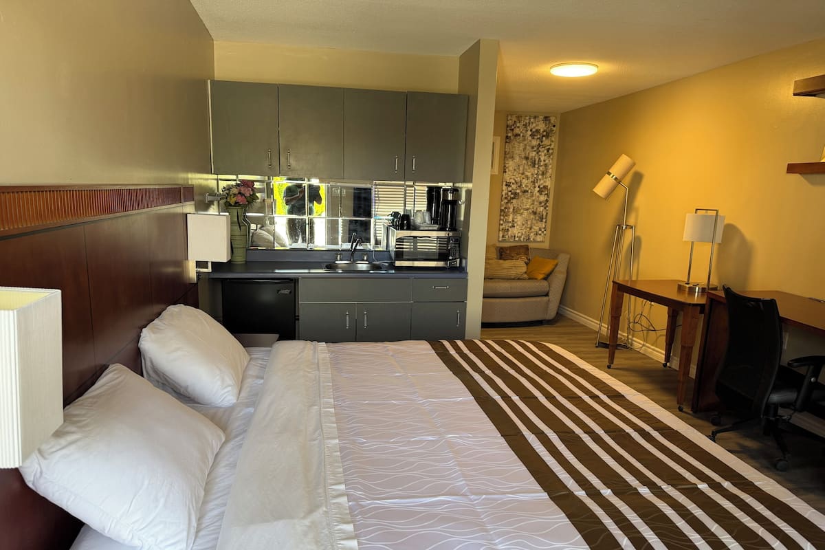 A hotel room with a bed, a desk, a chair, a kitchenette, and a sofa.