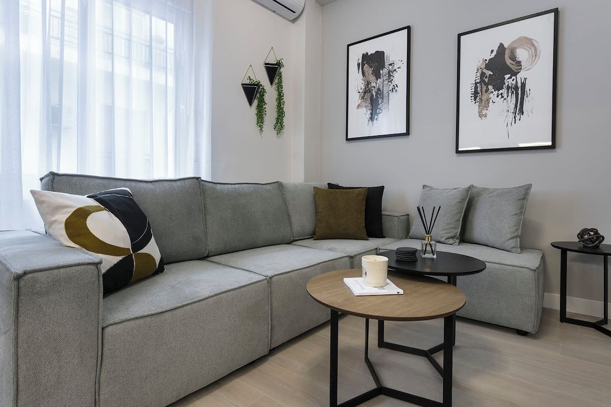 Un salon moderne avec un canapé d’angle gris, une table basse ronde et deux œuvres d’art encadrées accrochées au mur.