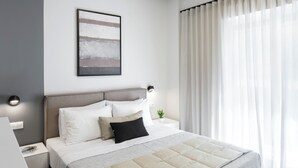 A modern hotel room with a large bed, bedside tables, a flat-screen TV, and a window with curtains. - Athenian Modern & Luxury Apartments (Vyronas)