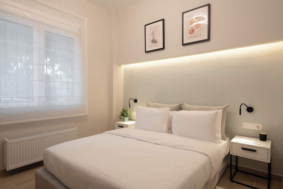 Une chambre à coucher comprenant un lit, des tables de chevet, une commode, une fenêtre avec des stores et des œuvres d’art accrochées au mur.