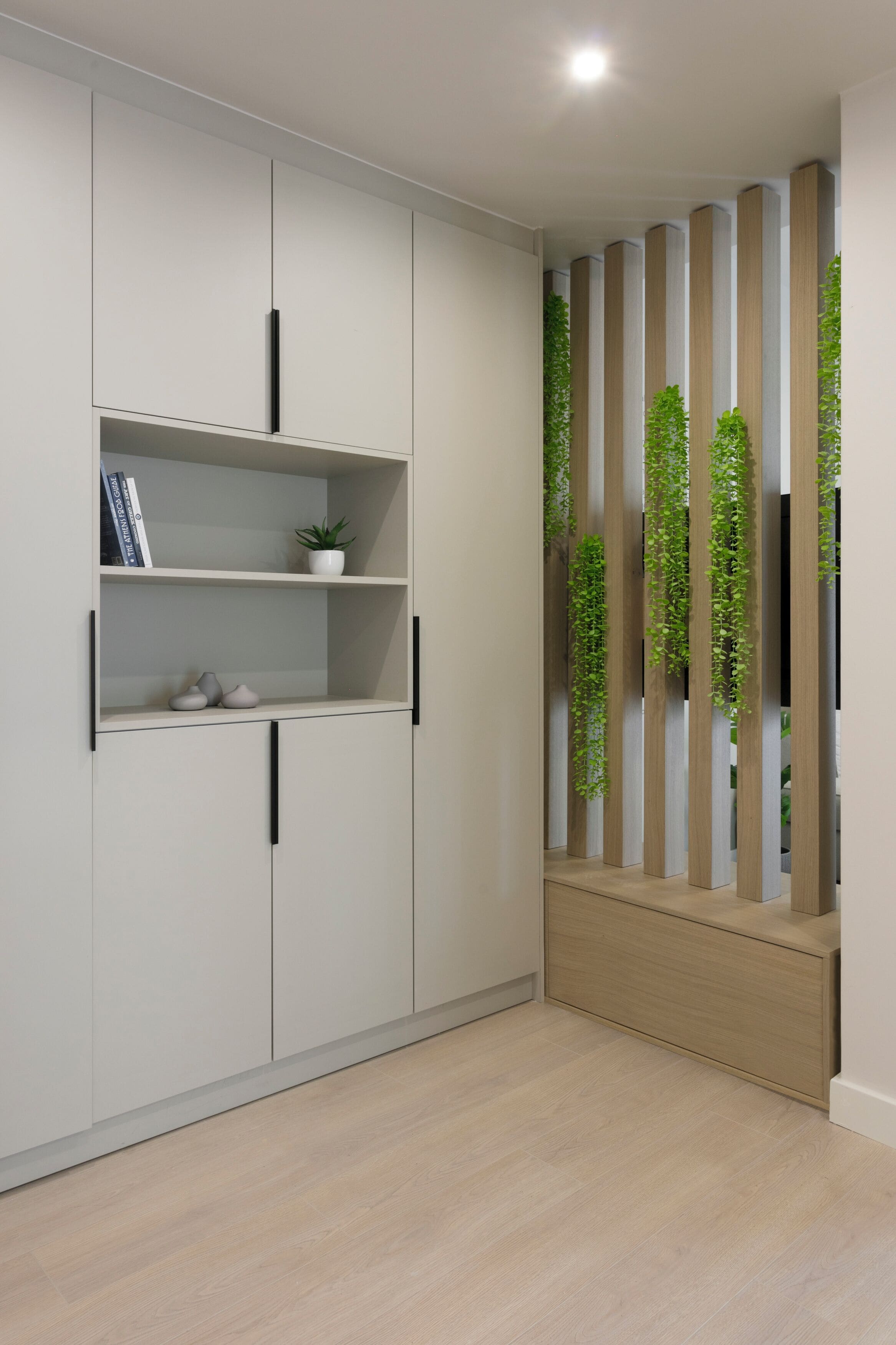Un interior moderno con un armario blanco, estanterías con libros y una planta, y un banco de madera con verdor vertical.
