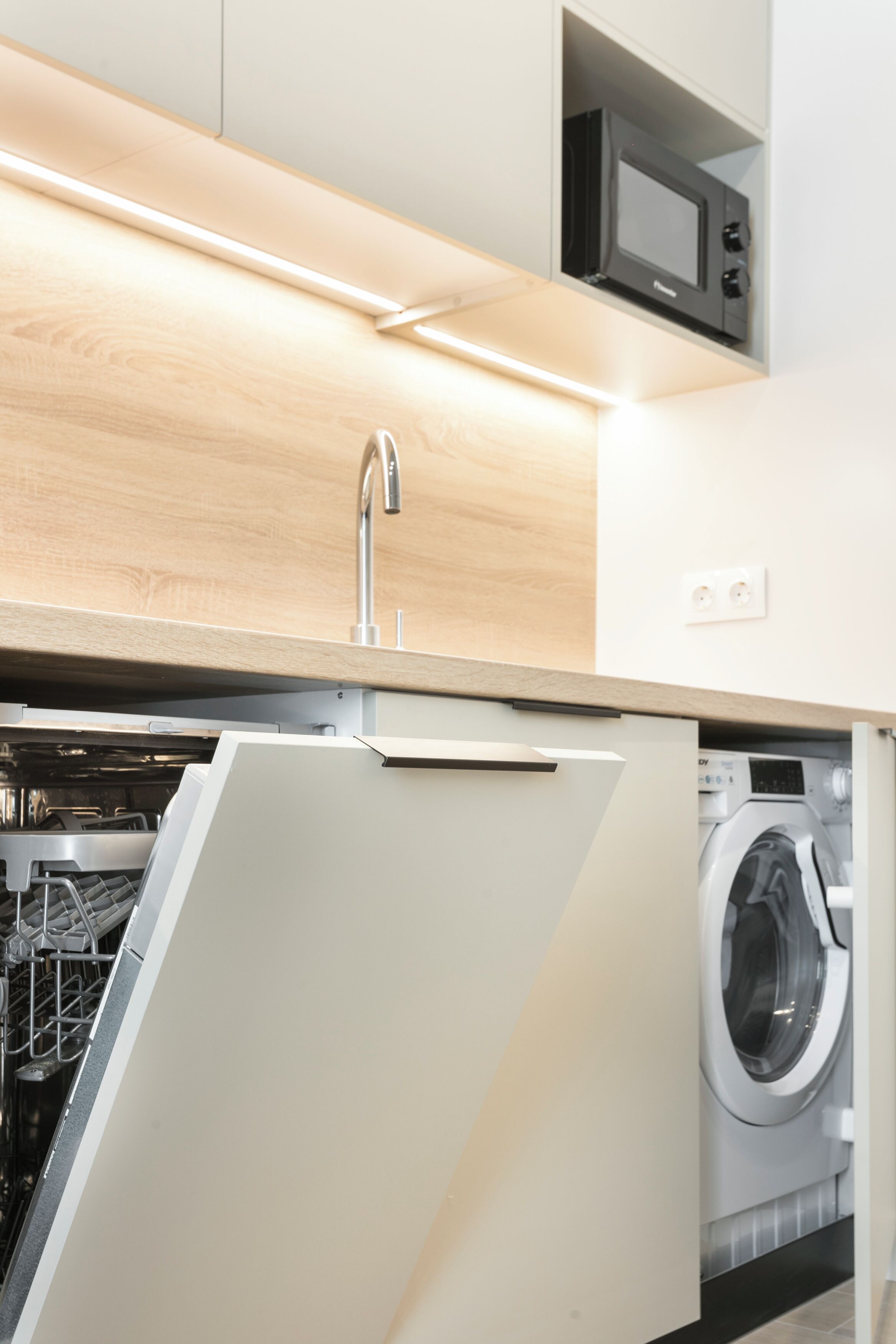 A modern kitchen with a dishwasher, washing machine, and a microwave.