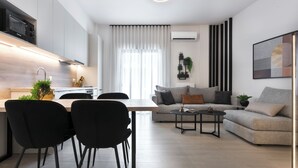 A modern living room with a sofa, a dining table with chairs, and a kitchen area with a microwave. - Athenian Modern & Luxury Apartments (Vyronas)