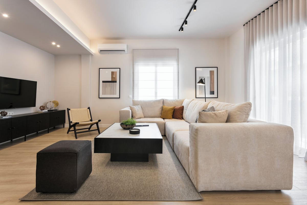 Un salon moderne avec un canapé, une table basse, un pouf noir, un téléviseur et des tableaux encadrés accrochés au mur.