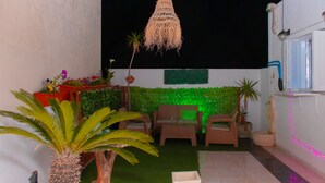 Un'area patio con erba sintetica, piante in vaso, mobili da esterno e illuminazione decorativa.