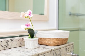 A bathroom with a marble countertop, a white textured planter with pink orchids, and a woven basket.