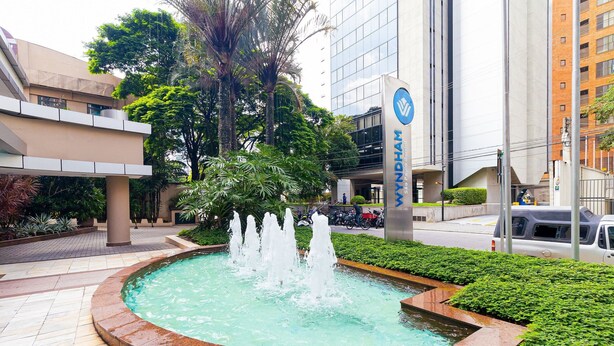A fountain surrounded by greenery, with a modern building in the background. - Vossa Bossa Berrini (São Paulo)
