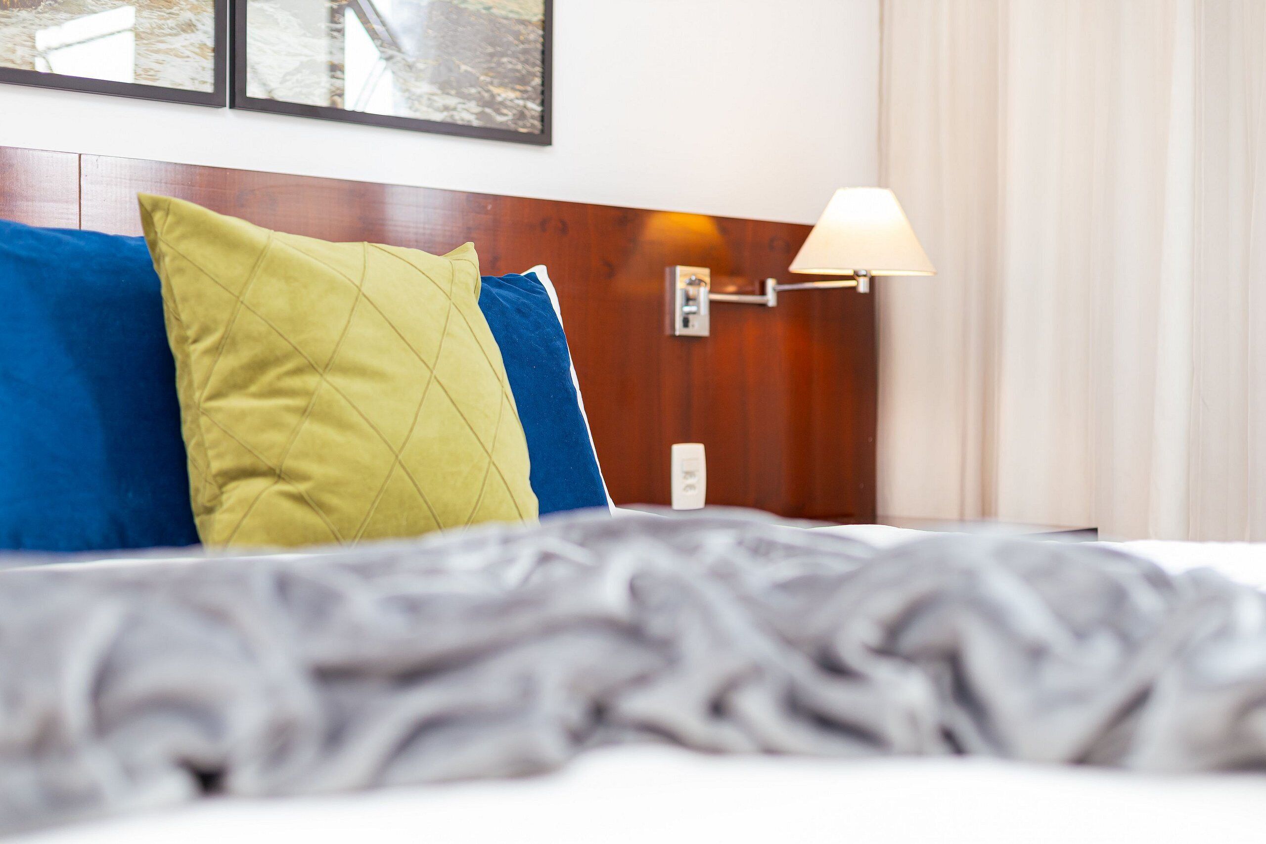 A hotel room with a bed, a nightstand, a lamp, and a wall-mounted thermostat.