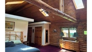 A log cabin bedroom with a bed, dresser, and a large window. - Wagonwheel Ranch (Viroqua)