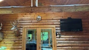 A log cabin with a wooden exterior, a glass door entrance, and a mounted deer head on the wall. - Wagonwheel Ranch (Viroqua)