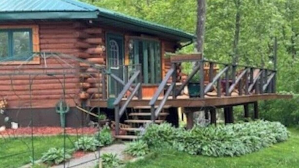 A rustic log cabin with a green roof, wooden deck, and a small porch. - Wagonwheel Ranch (Viroqua)