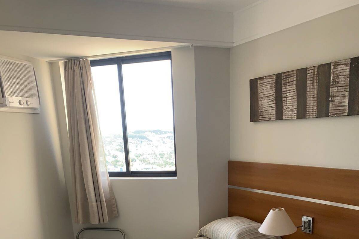 Et hotelværelse med to senge, et vindue med gardiner, en vægmonteret aircondition og en lampe.