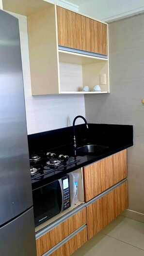A compact kitchen with a built-in stove, microwave, and black countertop. - CJC Short Stay Natal (Natal)