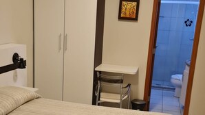 Ein Schlafzimmer mit einem Bett, einem Schreibtisch und einem Stuhl. Ein Badezimmer ist durch eine geöffnete Tür zu sehen.