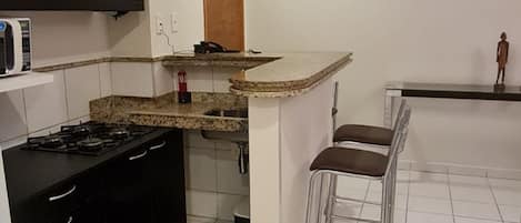 A compact kitchen with a microwave, stove, and bar stools.