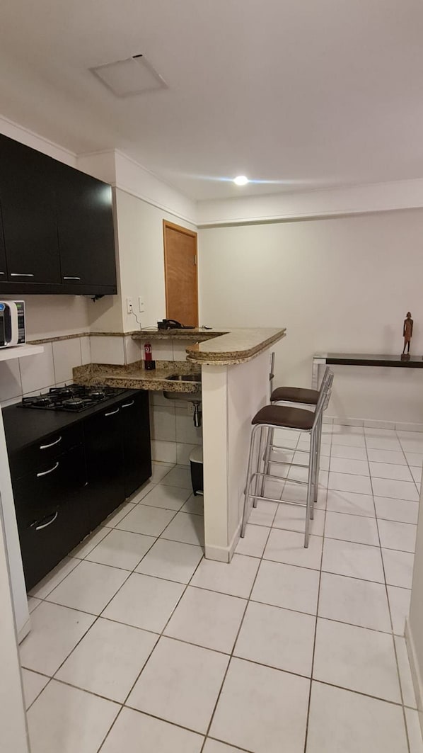 A compact kitchen with a microwave, stove, and bar stools. - CJC Short Stay Natal (Natal)