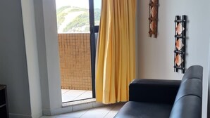 Ein Zimmer mit einer Schiebetür aus Glas, einem schwarzen Sofa, einer Pendelleuchte und einem wandmontierten Regal.