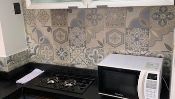 Uma cozinha com fogão a gás, micro-ondas, azulejos estampados e armários.