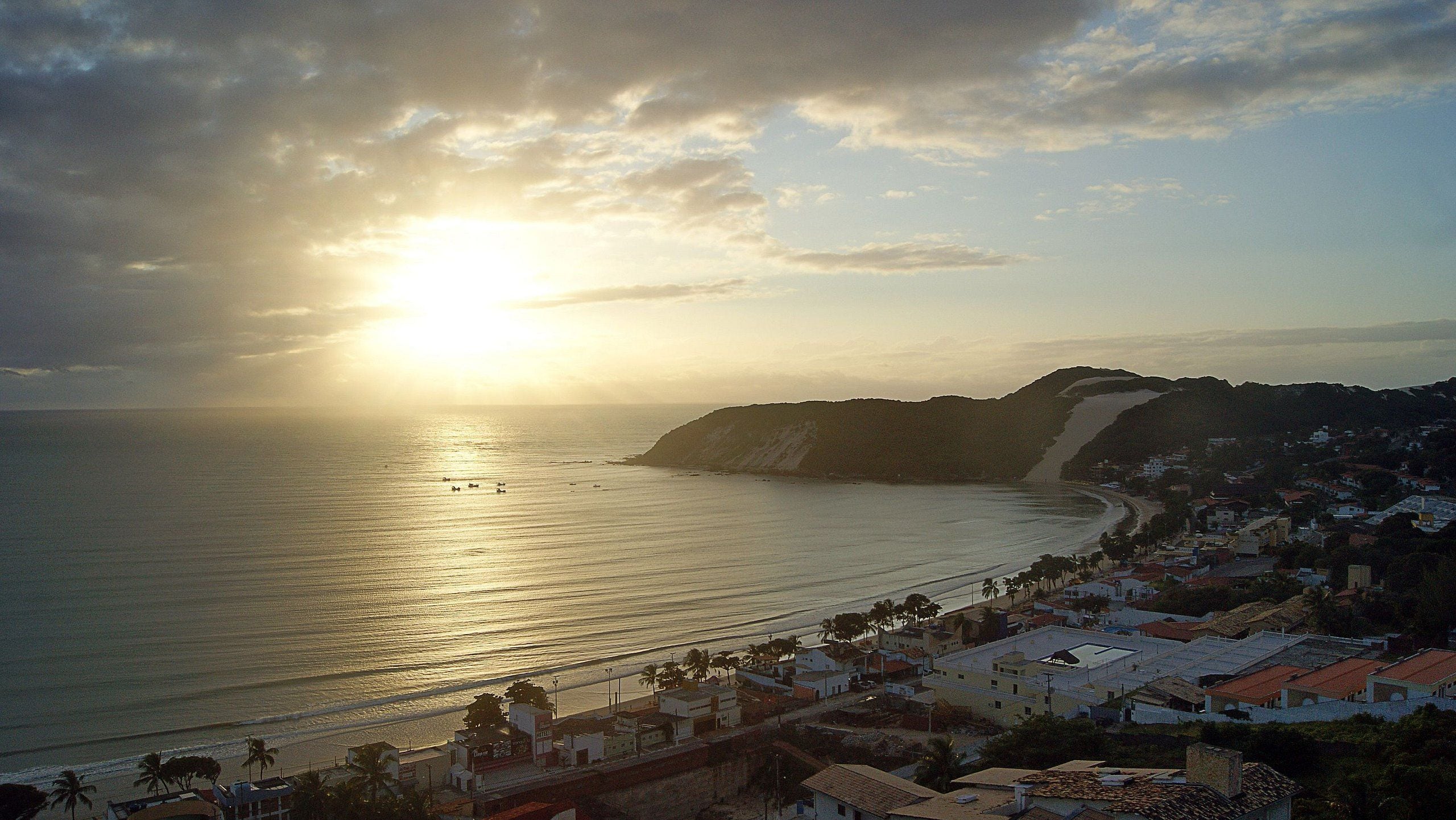 A coastal town with a beach, buildings, and a mountain in the background.