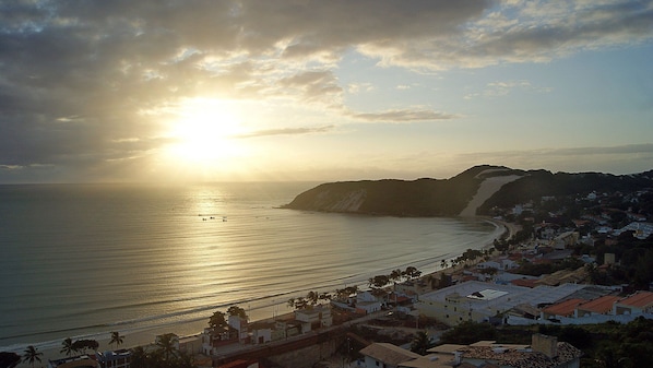 A coastal town with a beach, buildings, and a mountain in the background. - CJC Short Stay Natal (Natal)