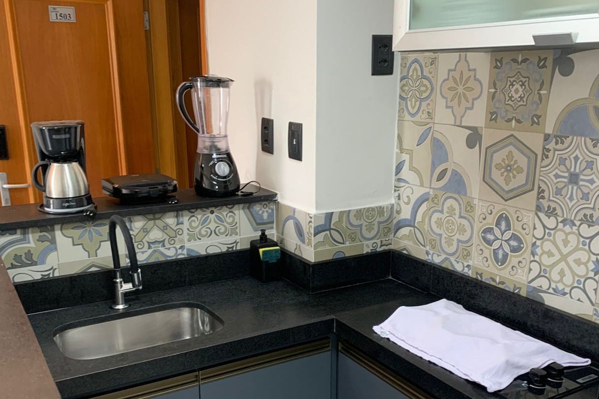 A kitchen with a coffee maker, blender, and a sink.