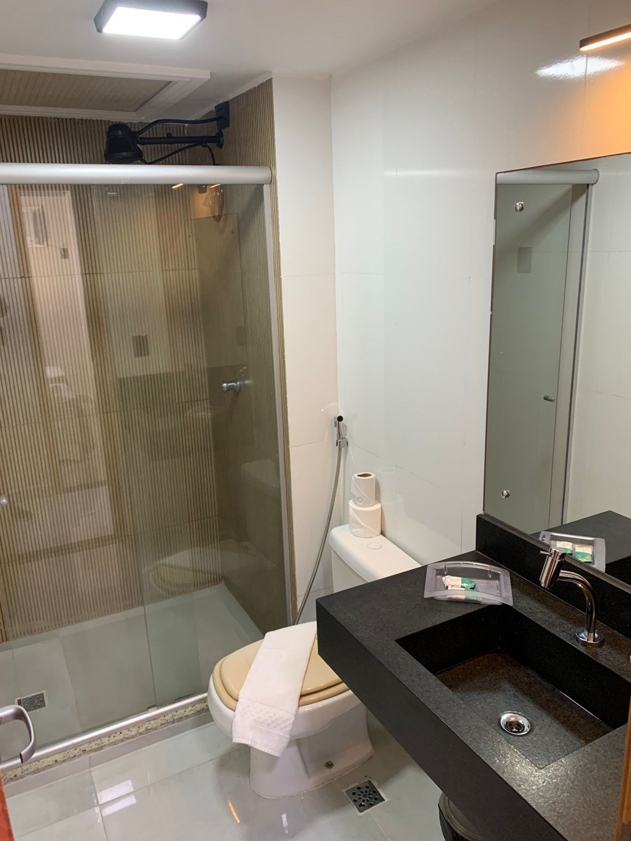A modern bathroom with a glass shower enclosure, a toilet with a towel, and a sink with a mirror.