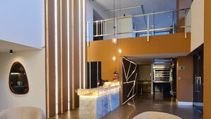A spacious lobby with a reception desk, two armchairs, a black round table, and a mezzanine level with a railing. - CJC Short Stay Natal (Natal)
