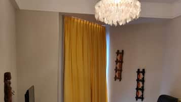 Sala de estar com sofá, televisão, mesa de vidro, lustre e cortina amarela.