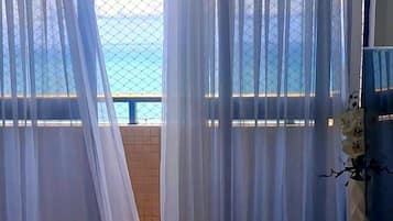 Una habitación con vistas a un balcón a través de cortinas translúcidas, un jarrón blanco y un cuenco sobre una consola blanca.