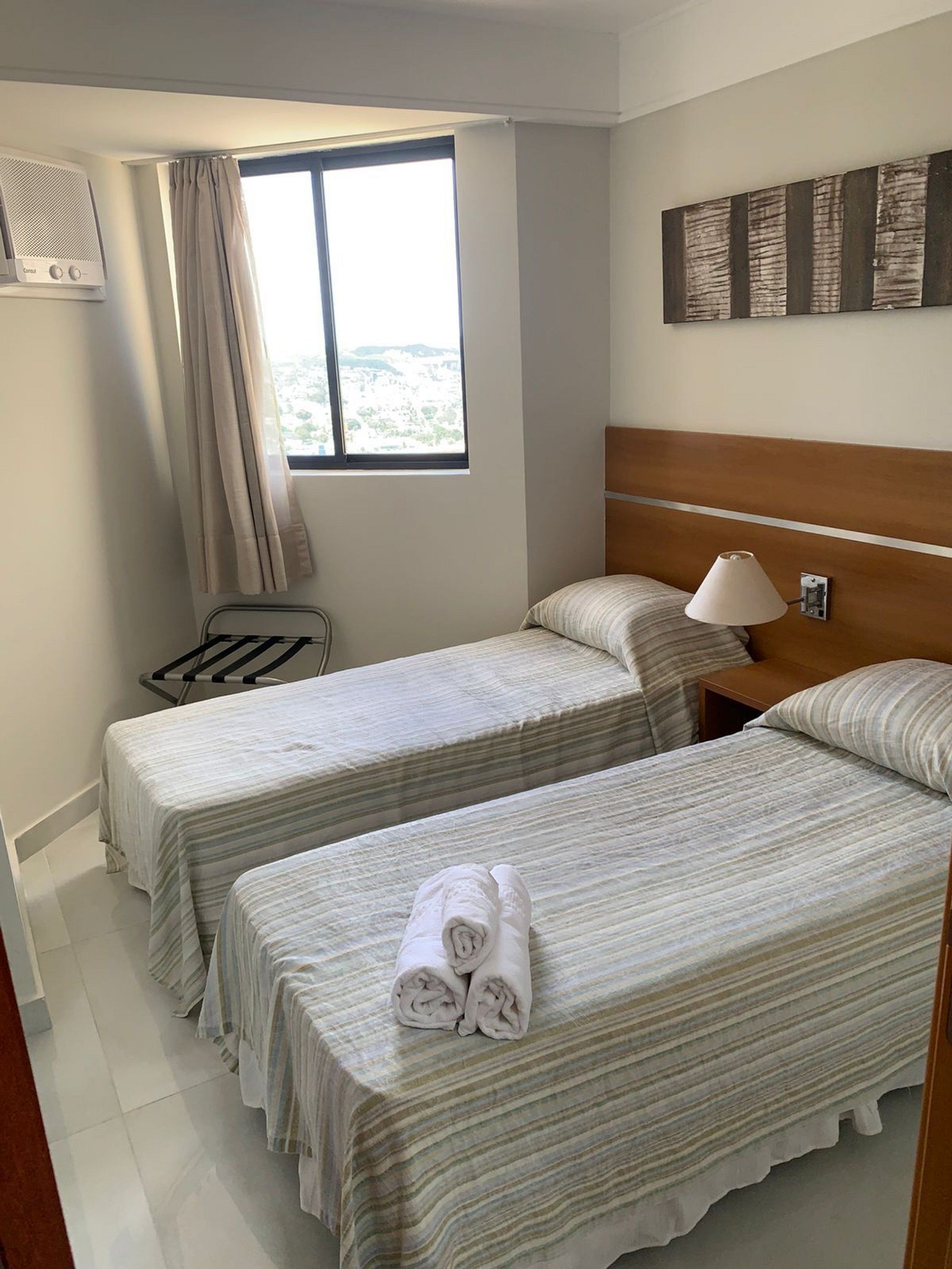 Una habitación de hotel con dos camas, una ventana con cortinas, aire acondicionado instalado en la pared y una lámpara.