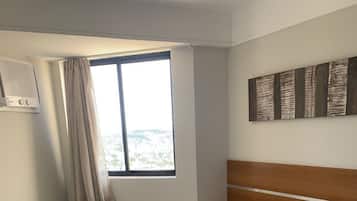 A hotel room with two beds, a window with curtains, a wall-mounted air conditioner, and a lamp.