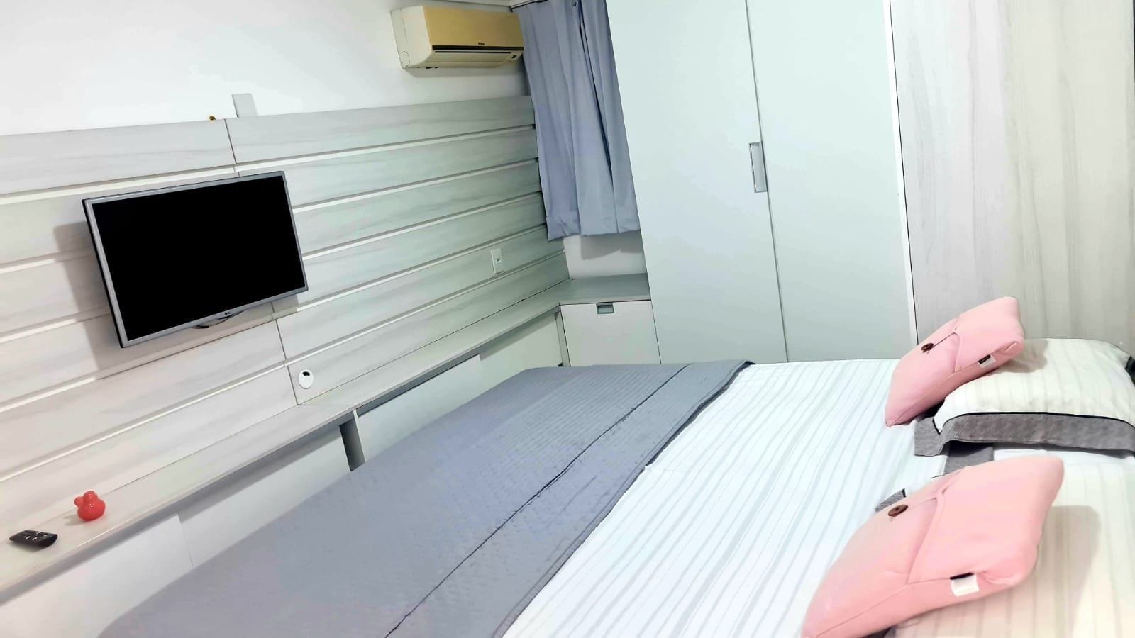 Habitación de hotel con cama, televisor montado en la pared, armario y una mesita con control remoto.