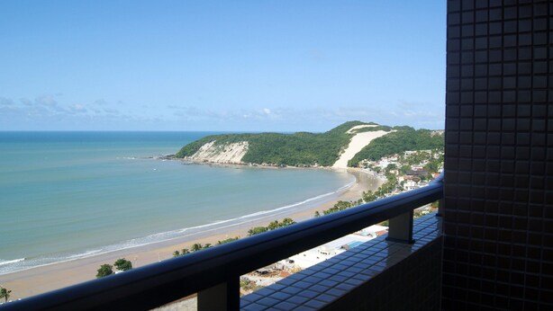 A coastal view with a beach, a cliff, and a residential area. - CJC Short Stay Natal (Natal)