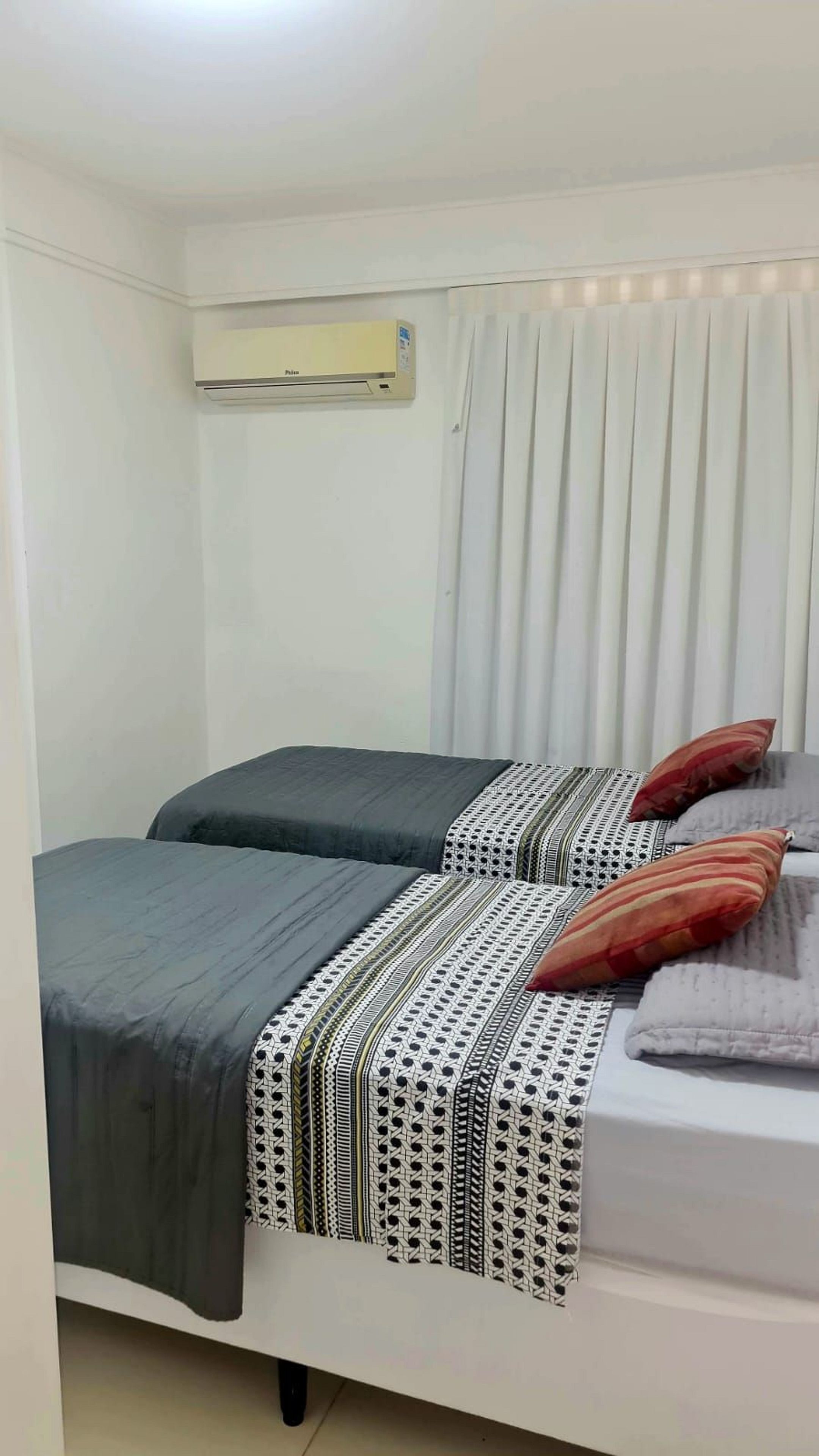 Ein Zimmer mit zwei Betten, einem fensterbelaubten Fenster und einer Klimaanlage.