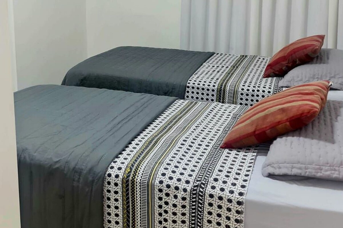 A room with two beds, a window with curtains, and an air conditioning unit.