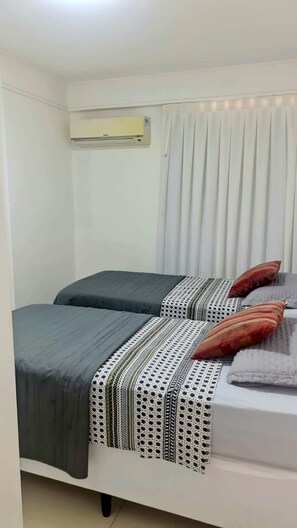 A room with two beds, a window with curtains, and an air conditioning unit. - CJC Short Stay Natal (Natal)